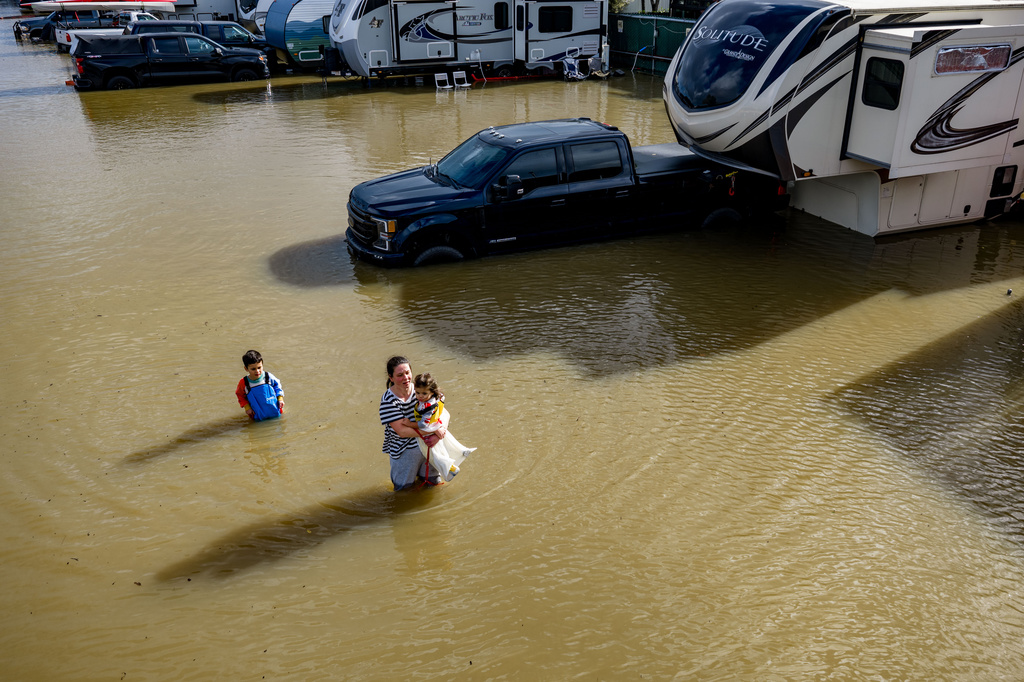 FILE - People wade through a recreational vehicle park flooded by a king tide on Jan. 3, 2026, near Corte Madera in Marin County, Calif. (AP Photo/Ethan Swope, File)