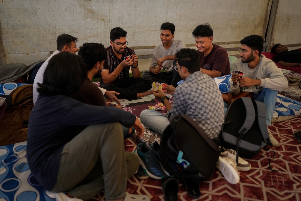 Stranded Indian travelers play cards as they sit inside a tent at a farmhouse owned by an Indian businessman, now converted into a shelter in Ajman, near Dubai, United Arab Emirates, Saturday, March 7, 2026. (AP Photo/Altaf Qadri)
