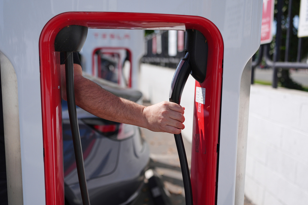 FILE - A person reaches to plug in an electric vehicle at a charging station May 22, 2025, in the City of Commerce, Calif. (AP Photo/Jae C. Hong, File)
