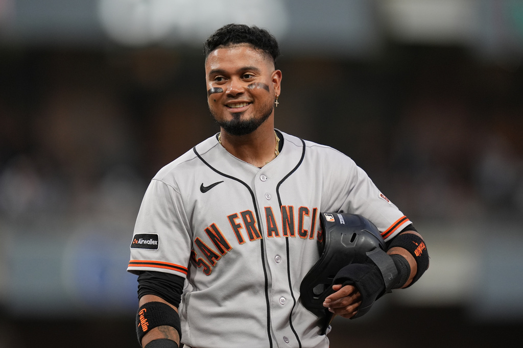 San Francisco Giants' Luis Arraez jokes with players in the San Diego Padres dugout as he stands on first base after getting hit by a pitch during the fourth inning of a baseball game Thursday, July 30, 2026, in San Diego. (AP Photo/Gregory Bull)