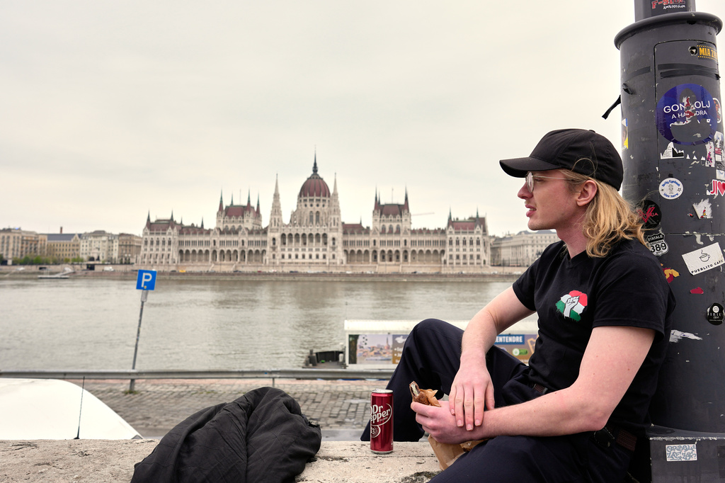 Milan, 26 years-old, relaxes by the Danube river, backdropped by the parliament building in Budapest, Hungary, Monday, April 13, 2026, after Peter Magyar's Tisza party defeated Prime Minister Viktor Orban's Fidesz party in the country's parliamentary elections. (AP Photo/Petr David Josek)