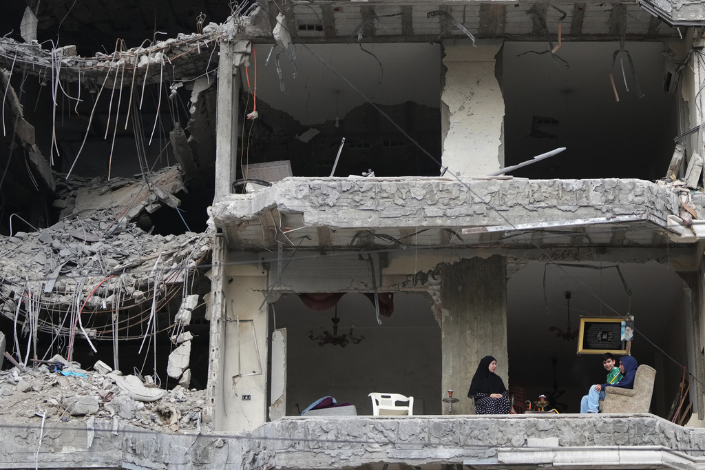 The wife and children of Fadi Al Zein, who lost both his homes in Israeli strikes in his village of Khiam and in Dahiyeh, sit on the balcony of their heavily damaged apartment building in Beirut's southern suburbs, Lebanon, Saturday, April 25, 2026. (AP Photo/Hassan Ammar)