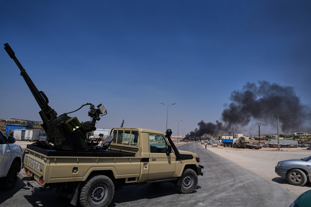 A pickup truck fitted with an anti-aircraft gun is parked across a road as smoke rises after an explosion at what state media said was a weapons depot in the Burj al-Nimra area near Sarmada, in Idlib province, Syria, Wednesday, Sept. 9, 2026.(AP Photo/Omar Albam)