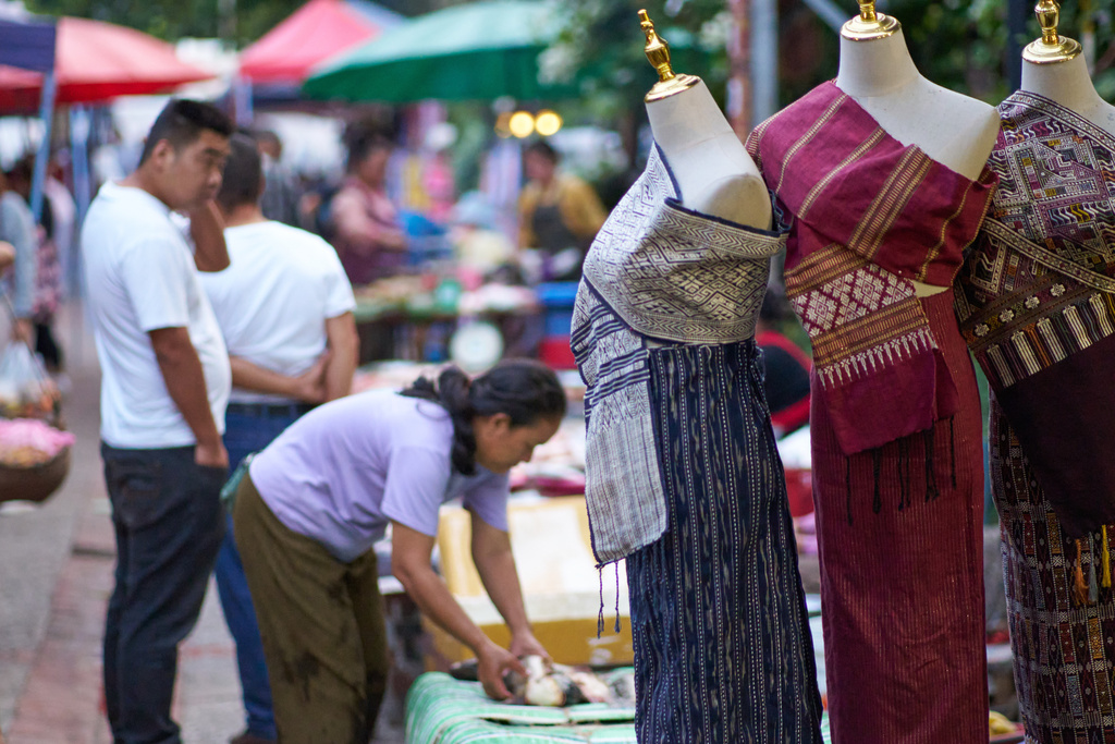 Traditional Lao outfits are displayed on mannequins as vendors and shoppers move through the night market in Luang Prabang, Laos, Monday, Nov. 3, 2025. (AP Photo/Eugene Hoshiko)