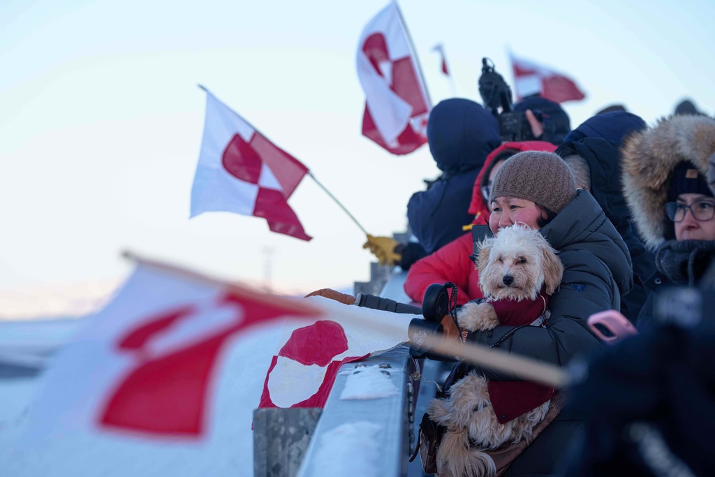 People wave national flags for Greenland Minister for Foreign Affairs and Research Vivian Motzfeldt as she arrives at the airport in Nuuk, Greenland, on Tuesday, Jan. 20, 2026. (AP Photo/Evgeniy Maloletka)