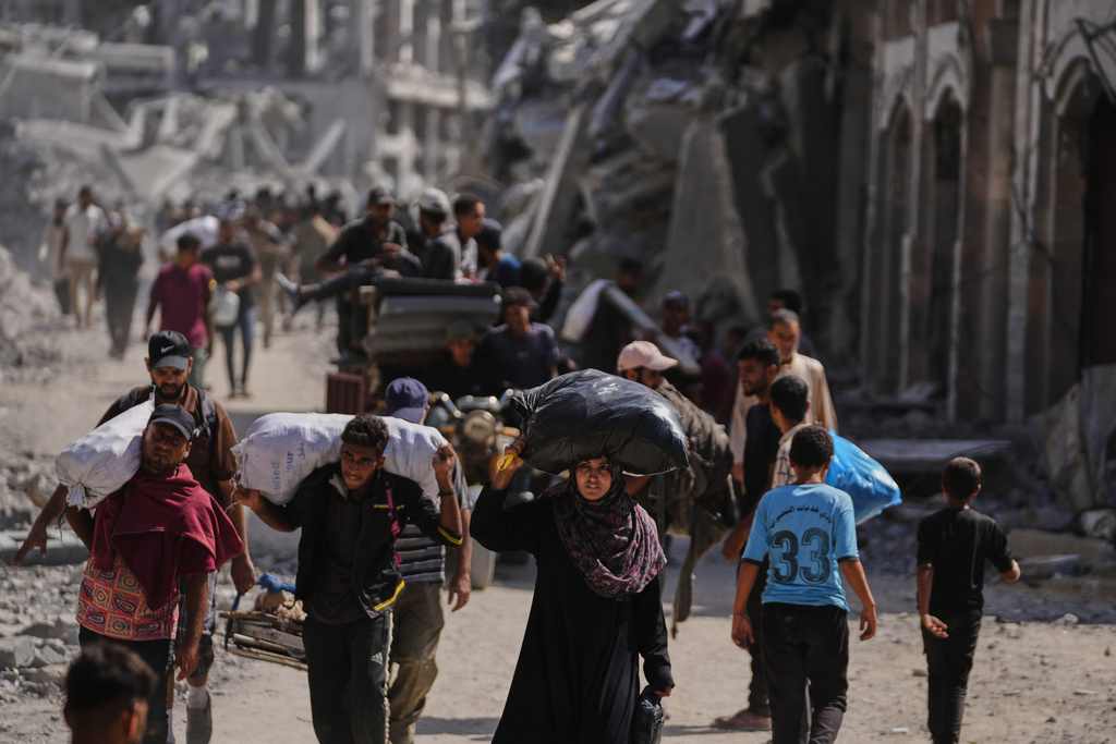 Displaced Palestinians walk with their belongings past destroyed buildings as they return to their homes in Khan Younis, southern Gaza Strip, Friday, Oct. 10, 2025, after Israel and Hamas agreed to a pause in their war and the release of the remaining hostages. (AP Photo/Jehad Alshrafi)
