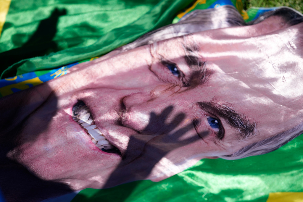 The shadow of a supporter of former President Jair Bolsonaro is cast on an image of him displayed outside the hospital where he was transported from prison for surgery the next day, in Brasilia, Brazil, Wednesday, Dec. 24, 2025. (AP Photo/Eraldo Peres)