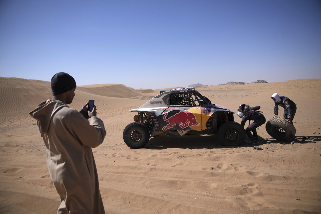 A man takes pictures of Goncalo Gurreiro and co-driver Cadu Sachs as they change a wheel during stage two of the Dakar Rally with start in Bisha and finish in Bisha, Saudi Arabia, Sunday, Jan. 5, 2025. (AP Photo/Christophe Ena)
