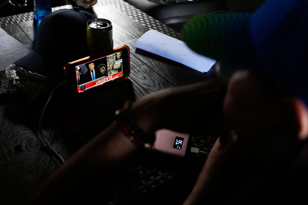 Government supporters watch on a smartphone a press conference by U.S. President Donald Trump explaining details of the operation in which U.S. forces captured and removed President Nicolás Maduro, in Caracas, Venezuela, Saturday, Jan. 3, 2026. (AP Photo/Ariana Cubillos)