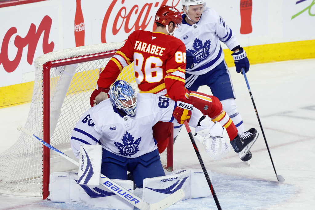 Calgary Flames' Joel Farabee, center, is pushed into Toronto Maple Leafs goalie Joseph Woll, left, by Maple Leafs' Troy Stecher, during first-period NHL hockey game action in Calgary, Alberta, Monday, Feb. 2, 2026. (Larry MacDougal/The Canadian Press via AP)