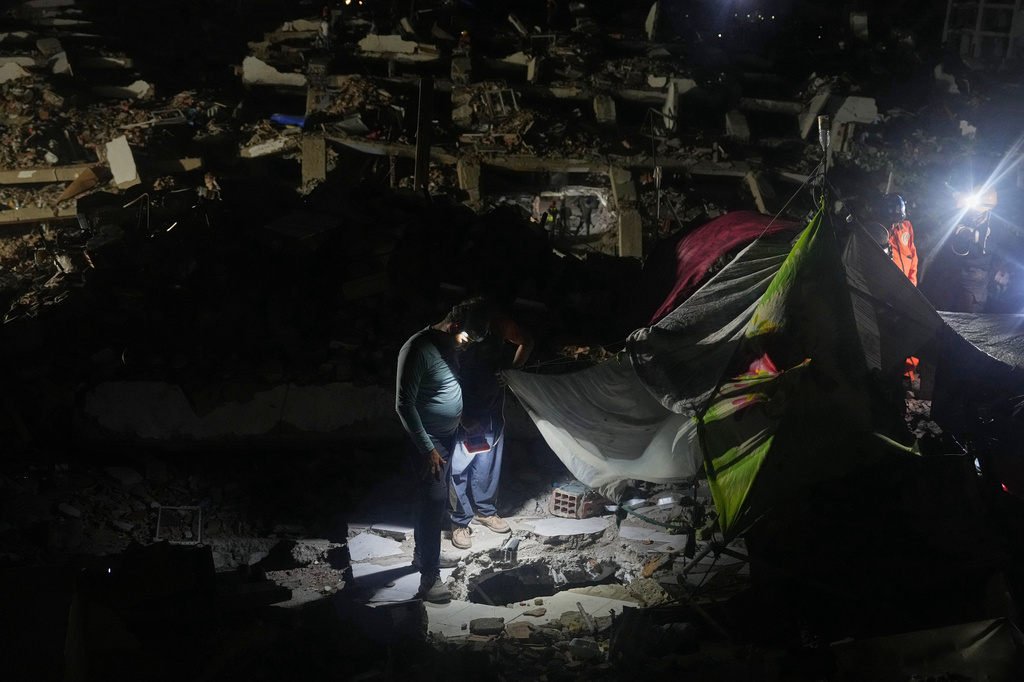 Jerfferson Cova, wearing a headlamp, looks at the deep hole he dug with other relatives in search of his mother-in-law, days after rescuing the bodies of his two children from a building collapsed by an earthquake in La Guaira, Venezuela, Tuesday, July 21, 2026. (AP Photo/Ariana Cubillos)