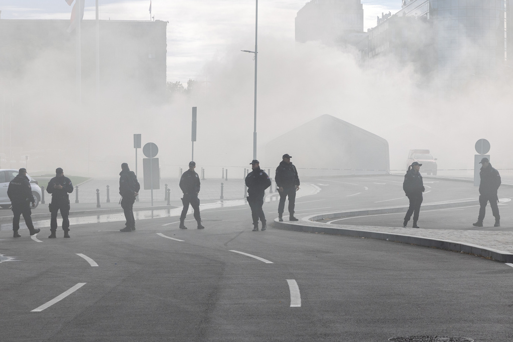 Police officers stand on a street as a fire is localized inside the government supporters' camp outside the Serbian parliament in Belgrade, Serbia, Wednesday, Oct. 22, 2025. (AP Photo/Marko Drobnjakovic)