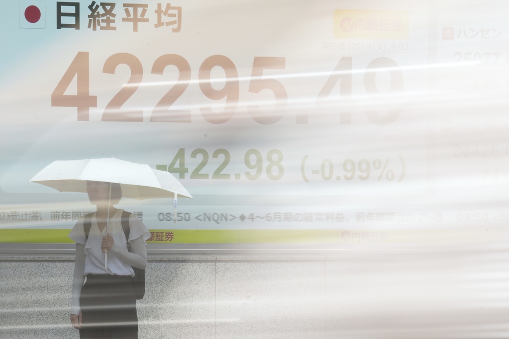 A person stands in front of an electronic stock board showing Japan's Nikkei index at a securities firm as a vehicle passes by on Monday, Sept. 1, 2025, in Tokyo. (AP Photo/Eugene Hoshiko)