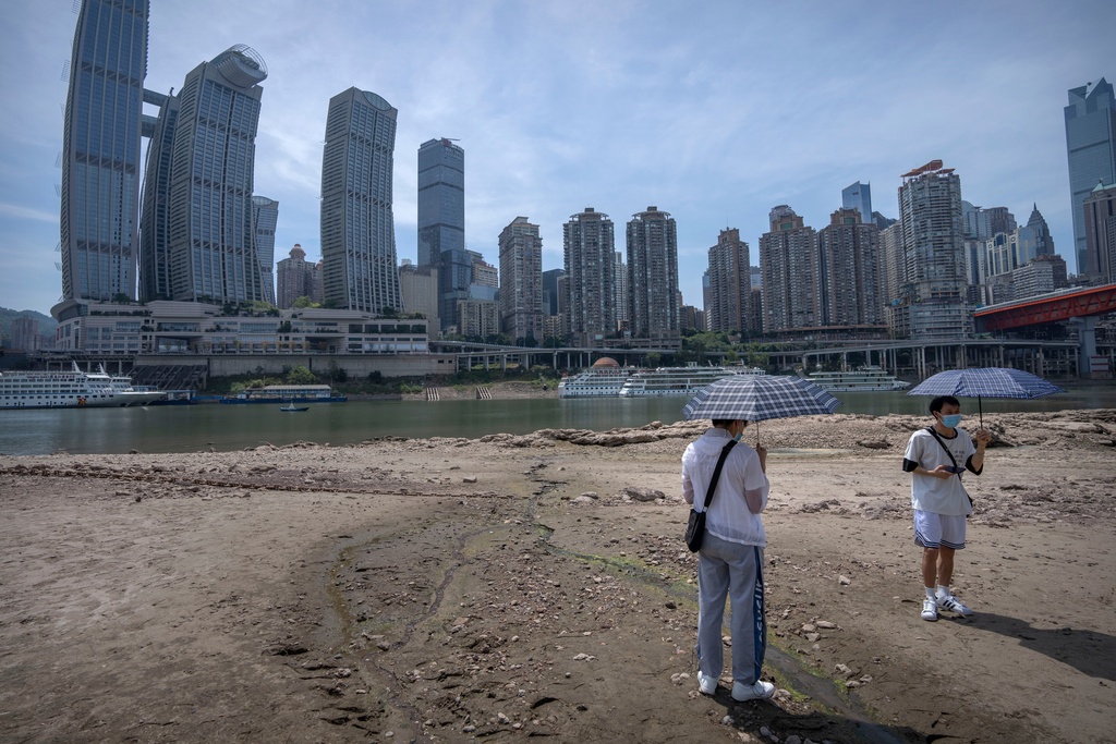 FILE - Students carrying umbrellas stand on the dry riverbed of the Jialing Rivera, a tributary of the Yangtze, in southwestern China's Chongqing Municipality, Aug. 19, 2022. (AP Photo/Mark Schiefelbein, File)