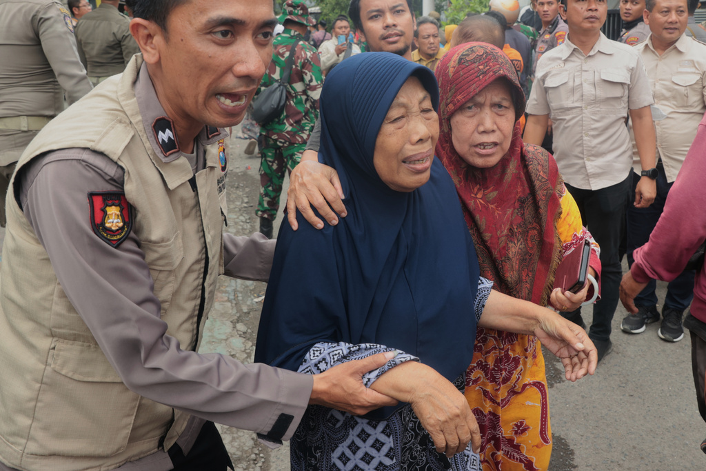A police officer assists a woman to walk away after a building collapsed at an Islamic boarding school in Sidoarjo, East Java, Indonesia, Tuesday, Sept. 30, 2025. (AP Photo/Trisnadi)