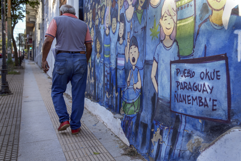 A pedestrian walks past a mural that says in the Guarani language "pueblo okue, Paraguay ñanemba'e" which means "People are moving. Paraguay is ours" in Asuncion, Friday, Aug. 22, 2025. (AP Photo/Jorge Saenz)
