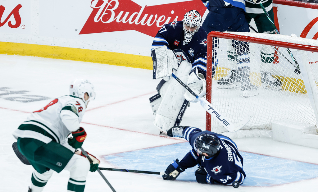 Winnipeg Jets' Dylan Samberg (54) blocks a shot by Minnesota Wild's Nico Sturm (78) as Jets goaltender Connor Hellebuyck (37) gets caught out of his net during third-period NHL hockey game action in Winnipeg, Manitoba, Saturday, Dec. 27, 2025. (John Woods/The Canadian Press via AP)