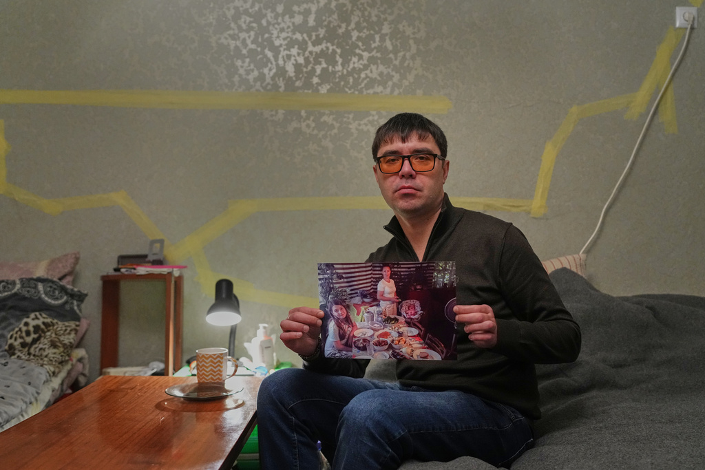 Yaroslav Nehoda, 40, holds a photograph of his niece, from left, wife and daughter, who were killed in a Russian drone attack on their house, as he sits in the temporary home he's living in, Thursday, Feb. 19, 2026, in Kyiv region, Ukraine. (AP Photo/Sergei Grits)