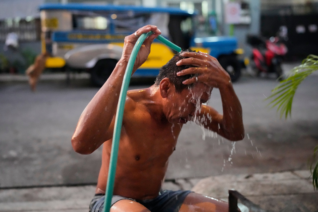 Jeepney driver Edgar Funelas bathes outside along a street near the jeepney where he and his 10-year-old daughter live in Quezon City, Philippines, on Friday April 10, 2026. (AP Photo/Aaron Favila)