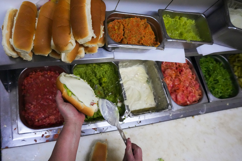 A cook prepares "completos", traditional Chilean hot dogs topped with mashed avocado, diced tomatoes and mayonnaise, at a restaurant in Santiago, Chile, Monday, Sept. 14, 2026. (AP Photo/Esteban Félix)