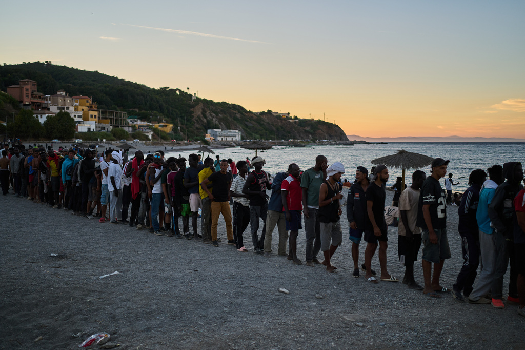 Migrantes que cruzaron desde Marruecos a España hacen fila para recibir comida en una playa en el territorio español de Ceuta, el lunes 3 de agosto de 2026. (AP Foto/Bernat Armangue)