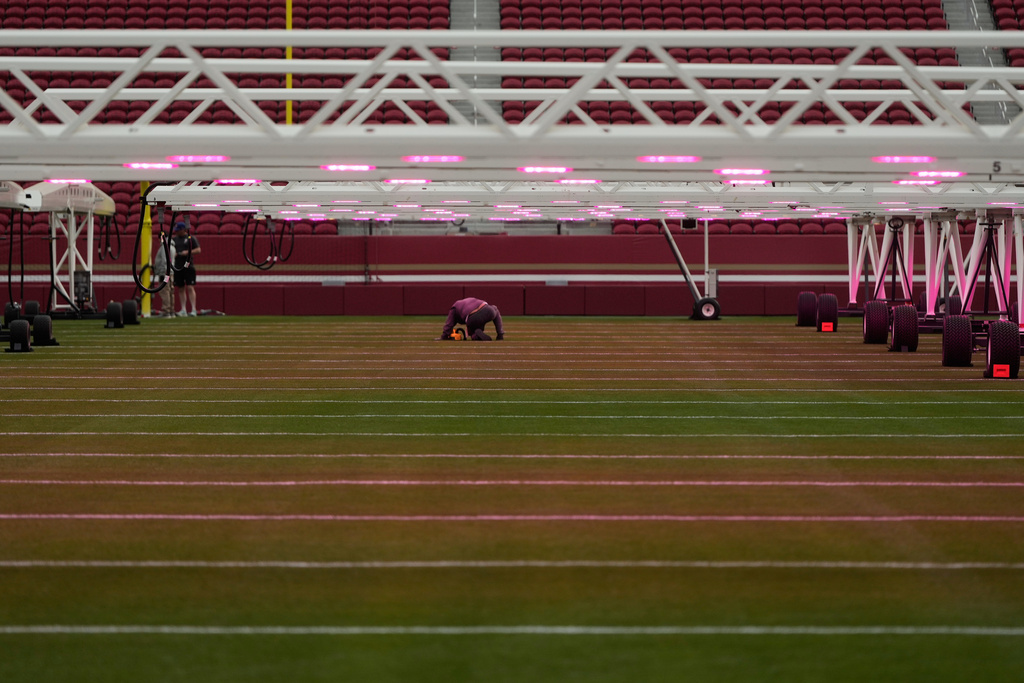 A worker kneels under grow lights on the field at Levi's Stadium as it is prepared for the NFL's Super Bowl LX football game in Santa Clara, Calif., Tuesday, Jan. 20, 2026. (AP Photo/Jeff Chiu)