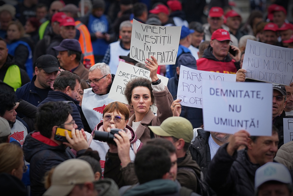 A woman holds a banner that reads "We want investments in the railway network" as trade union members protest against the government's austerity measures, outside Victoria Palace, the government headquarters, in Bucharest, Romania, Wednesday, Nov. 12, 2025. (AP Photo/Andreea Alexandru)