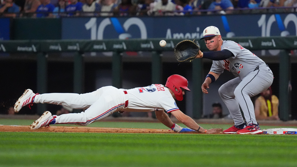 Texas Rangers' Evan Carter, left, dives to first base, beating a pickoff throw to Detroit Tigers first baseman Spencer Torkelson, right, during the second inning of a baseball game, Saturday, July 4, 2026, in Arlington, Texas. (AP Photo/LM Otero)