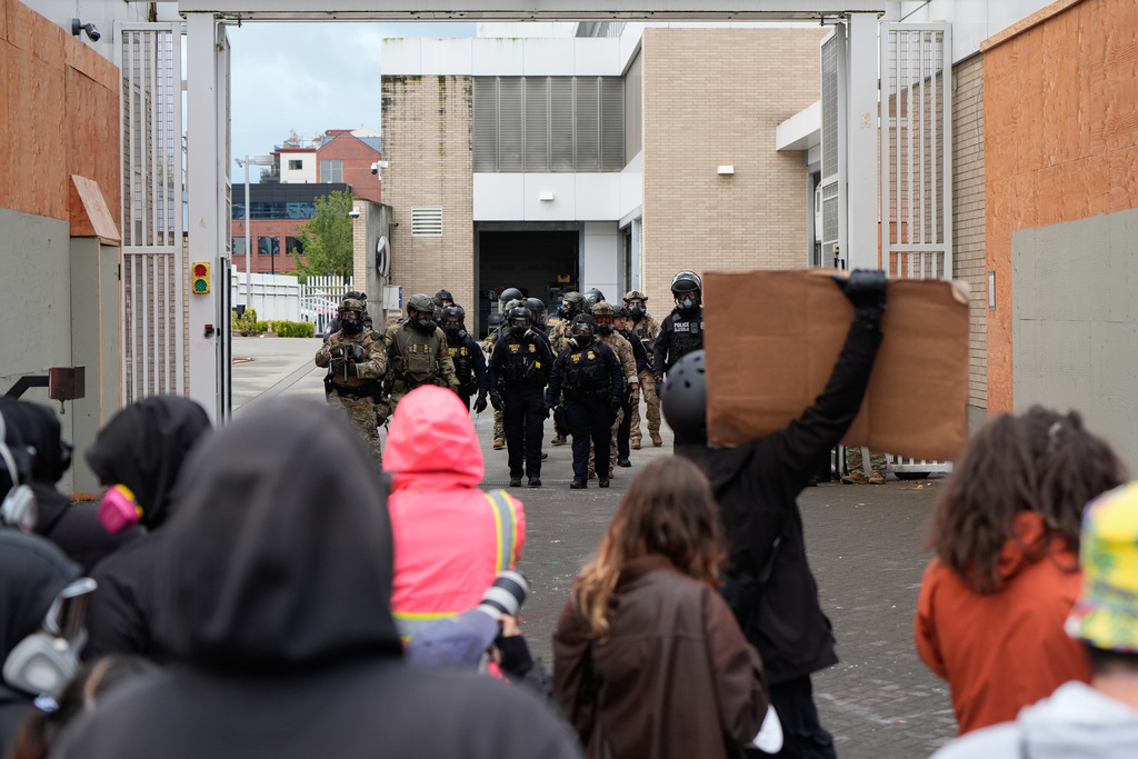 Law enforcement officers walk back to a U.S. Immigration and Customs Enforcement facility as people protest on Saturday, Oct. 11, 2025, in Portland, Ore. (AP Photo/Jenny Kane)