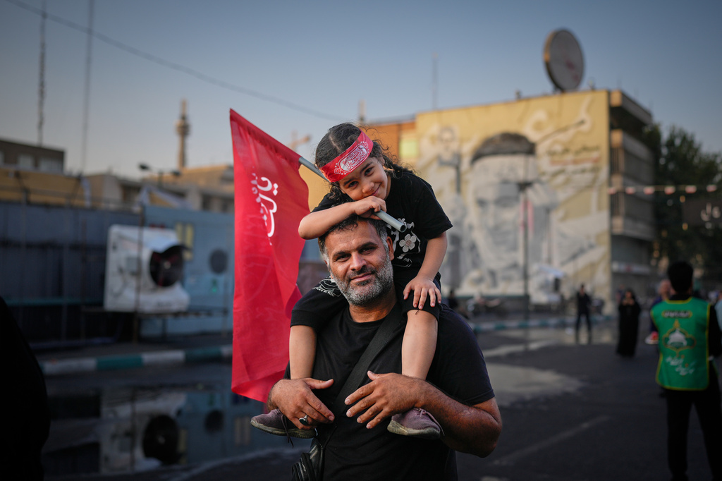 A man carries a child holding a red Shiite religious flag outside the Imam Khomeini Mosalla Grand Mosque during the funeral ceremonies for slain Iranian Supreme Leader Ayatollah Ali Khamenei and members of his family in Tehran, Iran, Saturday, July 4, 2026. (AP Photo/Altaf Qadri)