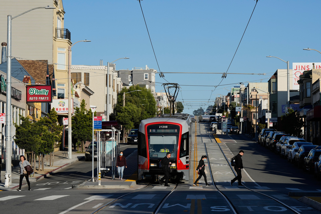 People cross Taraval Street after exiting a MUNI train in the Sunset District, Friday, Oct. 17, 2025, in San Francisco. (AP Photo/Godofredo A. Vásquez)