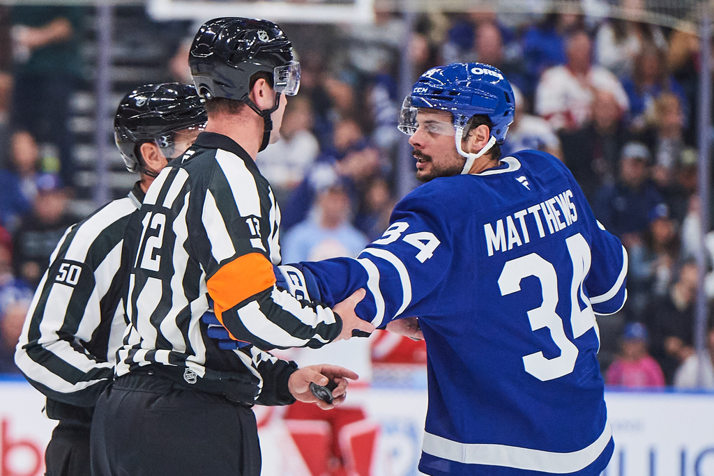 Toronto Maple Leafs' Auston Matthews (34) grabs on to an official after Simon Benoit (not shown) received a delay of game penalty during first period NHL hockey action in Toronto, Monday, Oct. 13, 2025. (Sammy Kogan/The Canadian Press via AP)