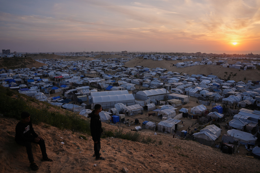 Palestinians youth look on as they stand in an area next to tents at a makeshift camp for displaced people, at sunset in Khan Younis, southern Gaza Strip, Thursday, April 9, 2026. (AP Photo/Abdel Kareem Hana)
