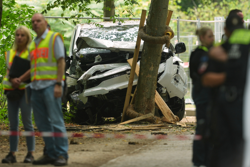 Police officers stand near a vehicle crashed into a tree after driving into a crowd near Berlin's annual Pride event, in Berlin, Germany, Sunday, July 26, 2026. (AP Photo/Markus Schreiber)