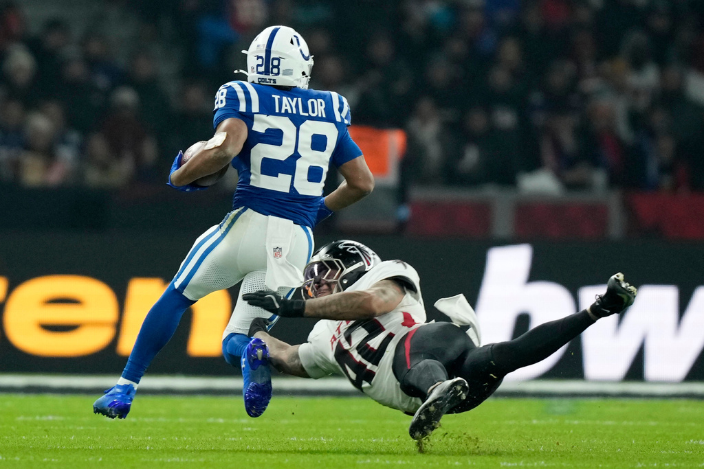 Indianapolis Colts running back Jonathan Taylor (28) tries to break a tackle by Atlanta Falcons linebacker Josh Woods (42) during the second half of an NFL football game, Sunday, Nov. 9, 2025, in Berlin, Germany. (AP Photo/Ebrahim Noorozi)