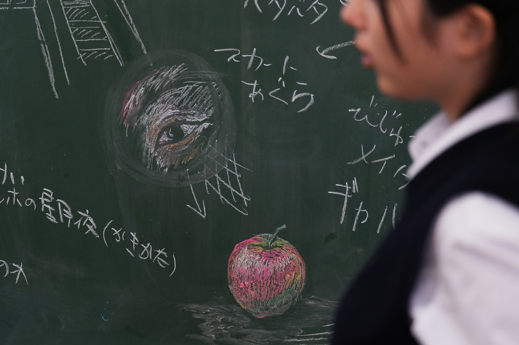 A member of the art club at Kumagaya Girls High School walks by chalk drawing designs on a blackboard at the school in Kumagaya, northwest of Tokyo, Tuesday, July 21, 2026, as they discuss their blackboard art design for its national contest. (AP Photo/Hiro Komae)