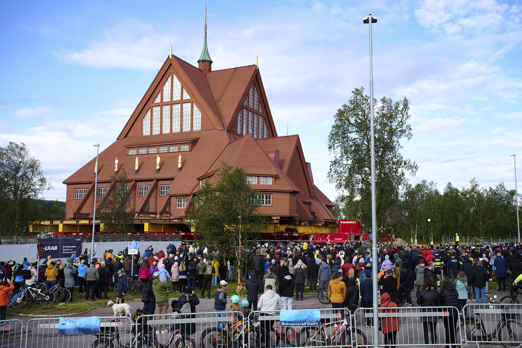 People gather outside the Kiruna Church, a Sami style wooden Swedish Lutheran church, called Kiruna Kyrka in Swedish, in Kiruna, Sweden, Tuesday, Aug. 19, 2025, as it is being moved along a 5-kilometer (3-mile) route east to a new city center as part of the town's relocation. (AP Photo/Malin Haarala)