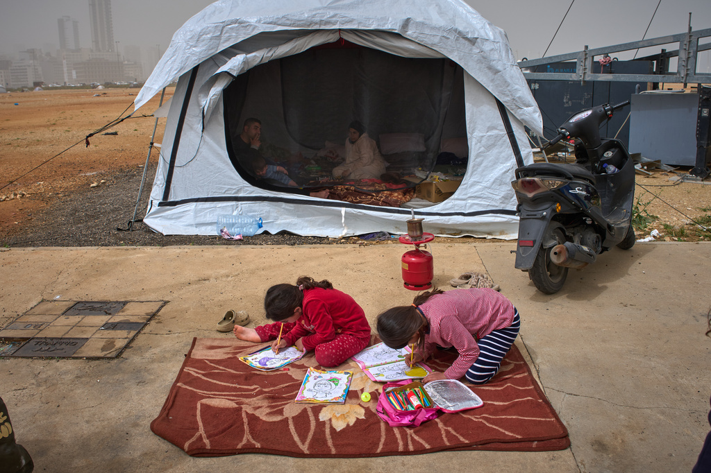 Tamara and her sister Amal color pictures on the floor as their parents, Sara and Ahmed, who fled their village of Khiyam in southern Lebanon due to Israeli bombardment, sit inside a tent used as a shelter in Beirut, Lebanon, Friday, April 3, 2026. (AP Photo/Emilio Morenatti)