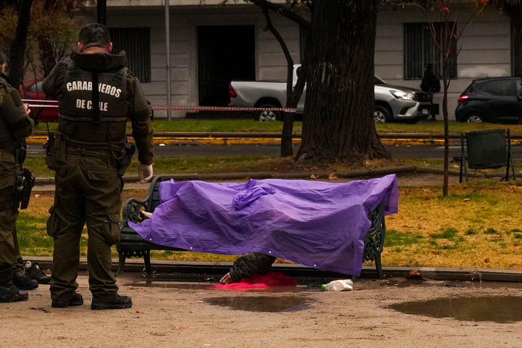 Police stand by a body on a park bench amid rainstorms in Santiago, Chile, Monday, July 20, 2026. The person died of hypothermia, according city officials. (AP Photo/Esteban Felix)