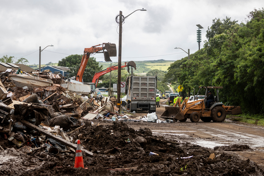 Excavators place debris onto trucks at a roundabout turned debris triage point by residents after the flood in Waialua, Hawaii Monday, March 23, 2026. (Stephen Lam/San Francisco Chronicle via AP)