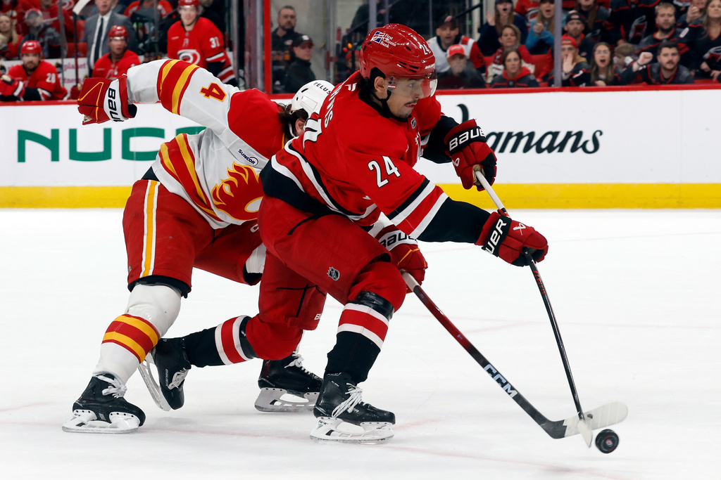 Carolina Hurricanes' Seth Jarvis (24) takes a shot with Calgary Flames' Rasmus Andersson (4) reaching in during the second period of an NHL hockey game in Raleigh, N.C., Sunday, Nov. 30, 2025. (AP Photo/Karl DeBlaker)