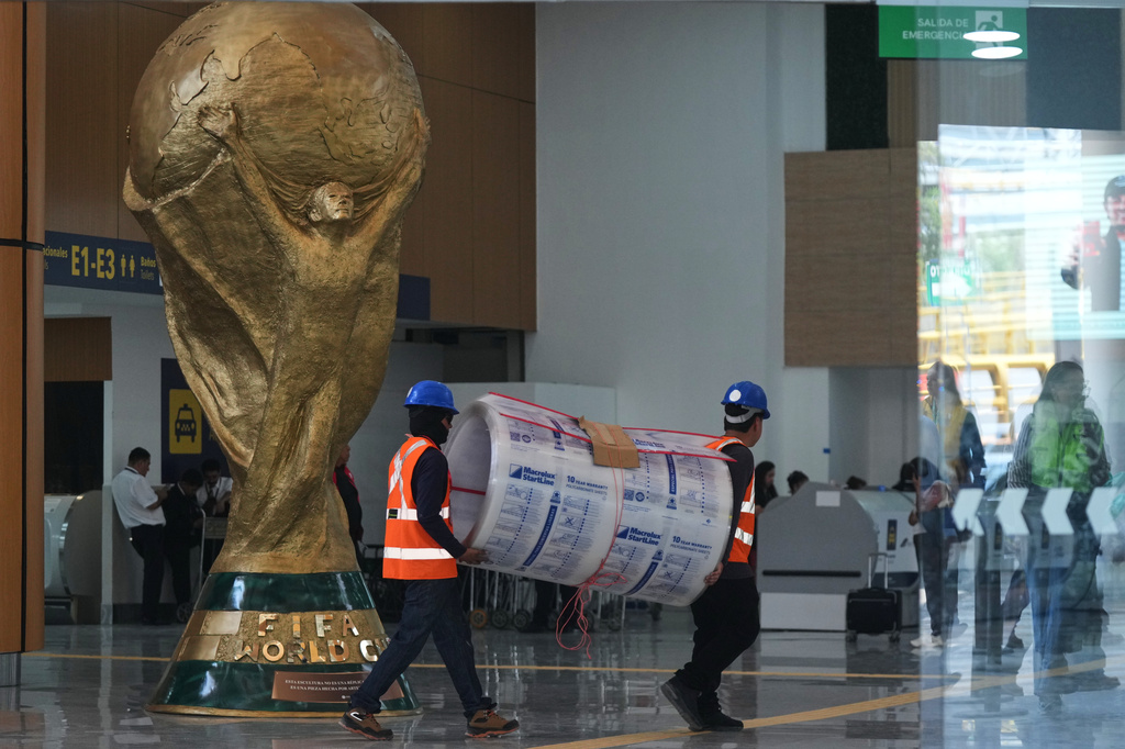 Workers transport a roll of foam next to the FIFA World Cup trophy during a guided media tour of the renovation site at Benito Juárez International Airport, in preparation for the 2026 World Cup, in Mexico City, on Tuesday, May 19, 2026. (AP Photo/Fernando Llano)