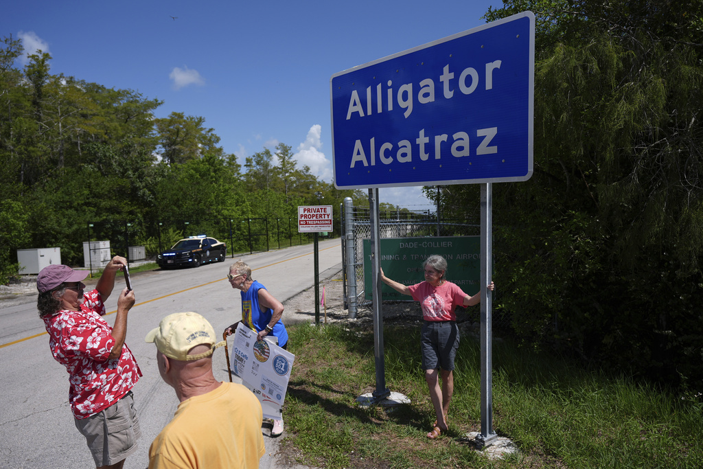 People take pictures in front of a sign reading "Alligator Alcatraz" as passerby, some opposed, some in support, visit the entrance to an immigration detention center in the Florida Everglades, Thursday, Aug. 28, 2025, in Collier County, Fla. (AP Photo/Rebecca Blackwell)
