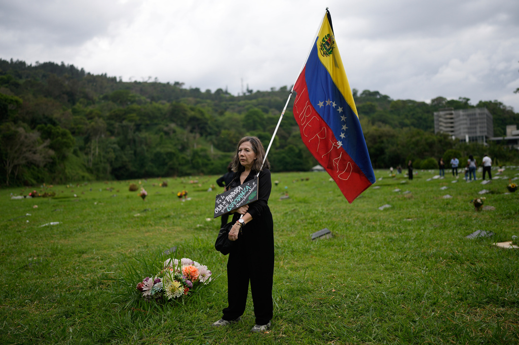 Rosibel Torres holds a Venezuelan flag during the burial of Carmen Navas, the mother of Victor Hugo Quero who Venezuelan authorities said died in custody following his arrest about a year earlier, in Caracas, Venezuela, Tuesday, May 19, 2026. (AP Photo/Ariana Cubillos)