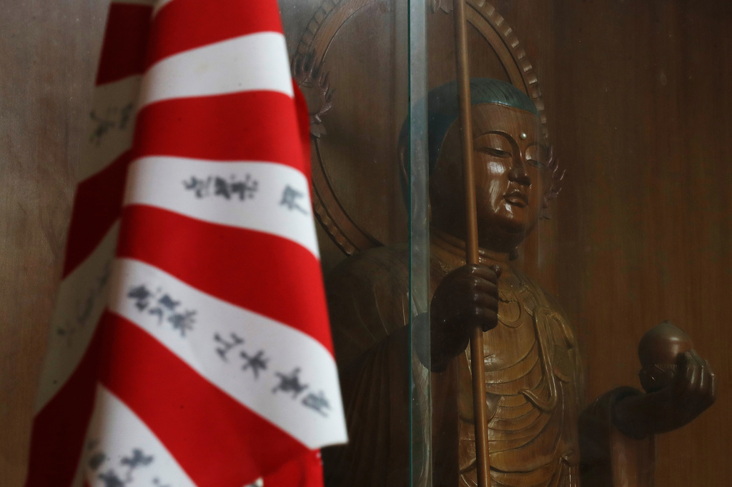 An old Japanese flag, also known as the Rising Sun Flag, is placed next to a Buddhist monk statue at Chaoyin Temple in Hengchun township, Pingtung county, southern Taiwan, Sunday, July 19, 2026. (AP Photo/Chiang Ying-ying)