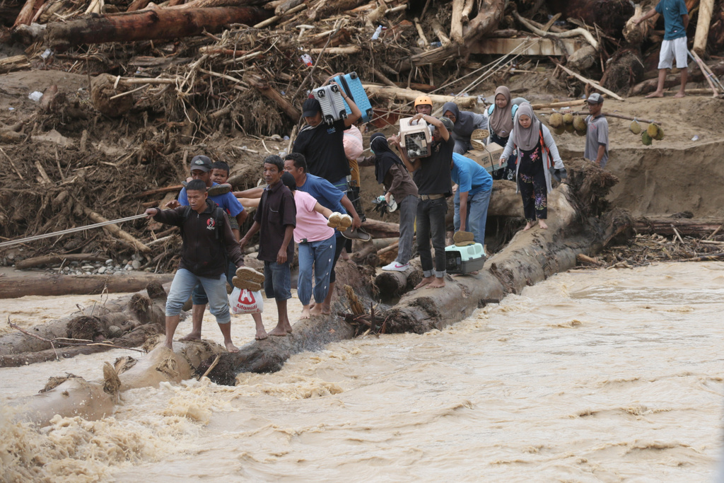 FILE - Flood survivors use logs to cross a river in Batang Toru, North Sumatra, Indonesia, Dec. 2, 2025. (AP Photo/Binsar Bakkara, File)