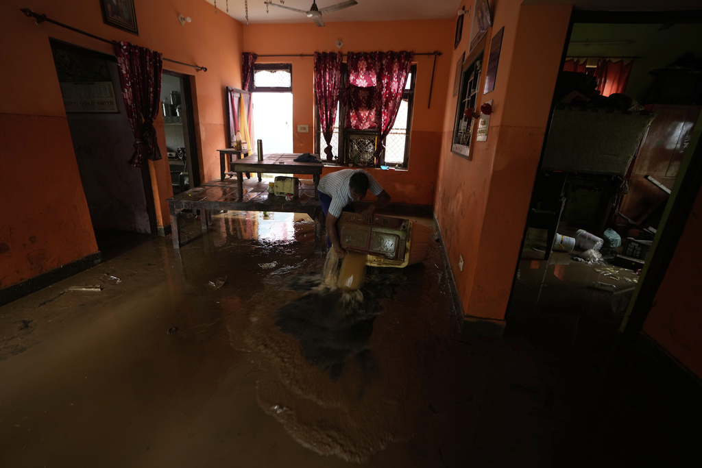 An Indian man drains water from a washing machine after flash floods hit the outskirts of Jammu, India, Sunday, Aug. 24, 2025.(AP Photo/Channi Anand)