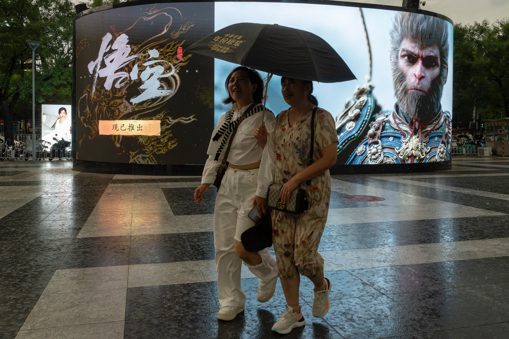 Women share an umbrella as they past an ad promoting the blockbuster Chinese video game "Black Myth: Wukong," in Beijing, Friday, Aug. 23, 2024. (AP Photo/Ng Han Guan)