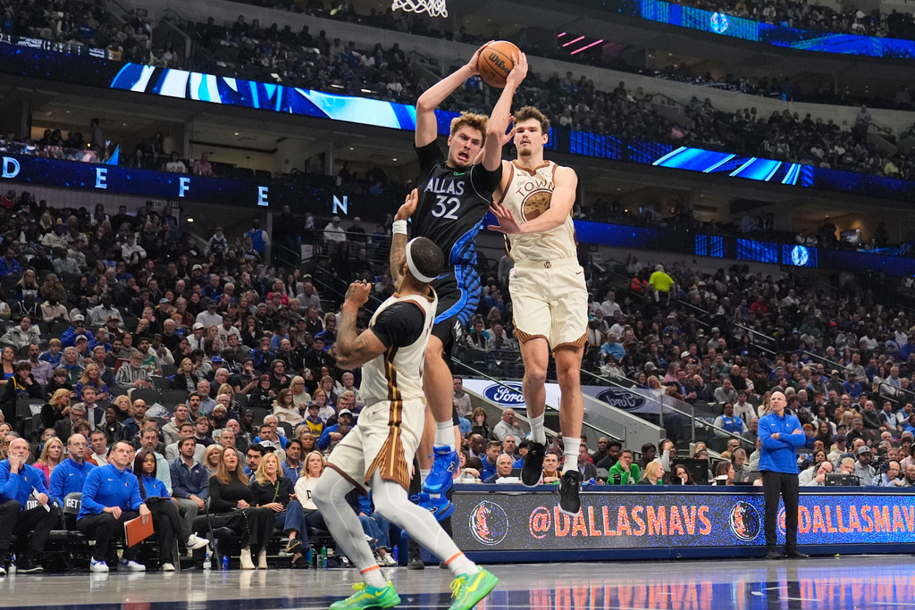 Dallas Mavericks forward Cooper Flagg (32) comes down with a rebound against Golden State Warriors' Gary Payton II, left, and Quinten Post, right, in the first half of an NBA basketball game in Dallas, Thursday, Jan. 22, 2026. (AP Photo/Tony Gutierrez)