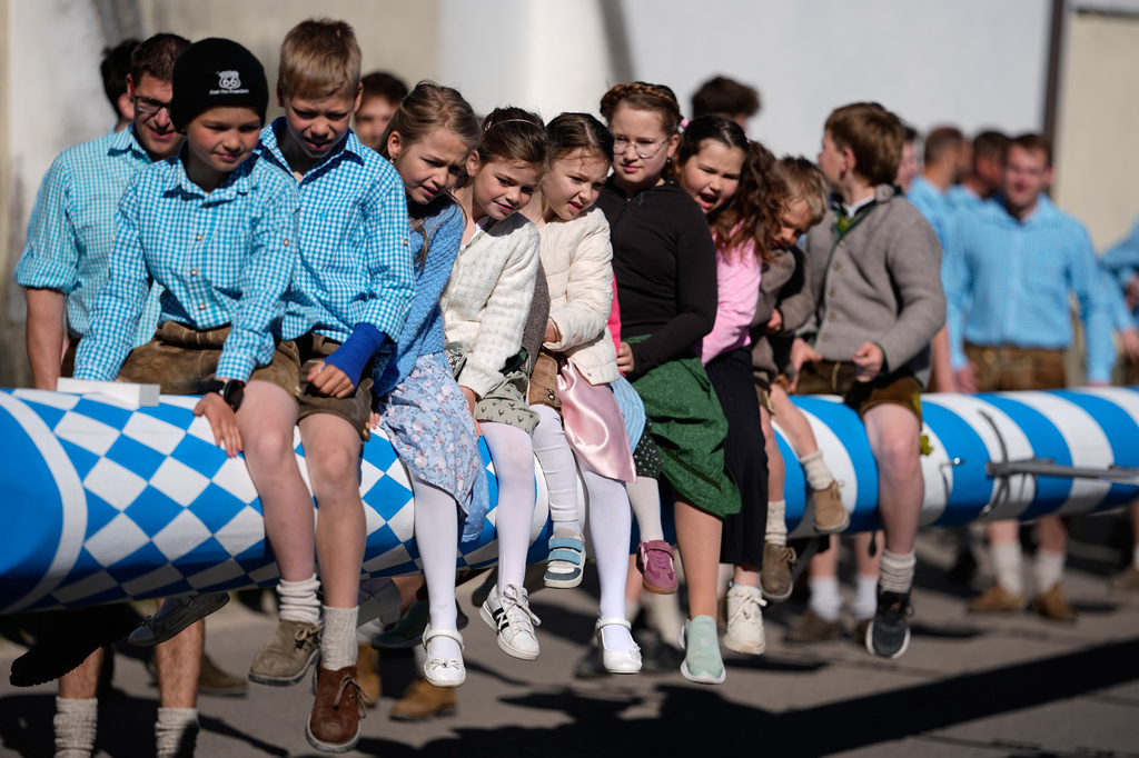 Young children sit on a May pole before it is erected in Kuehbach, Germany, Friday, May 1, 2026. (AP Photo/Matthias Schrader)